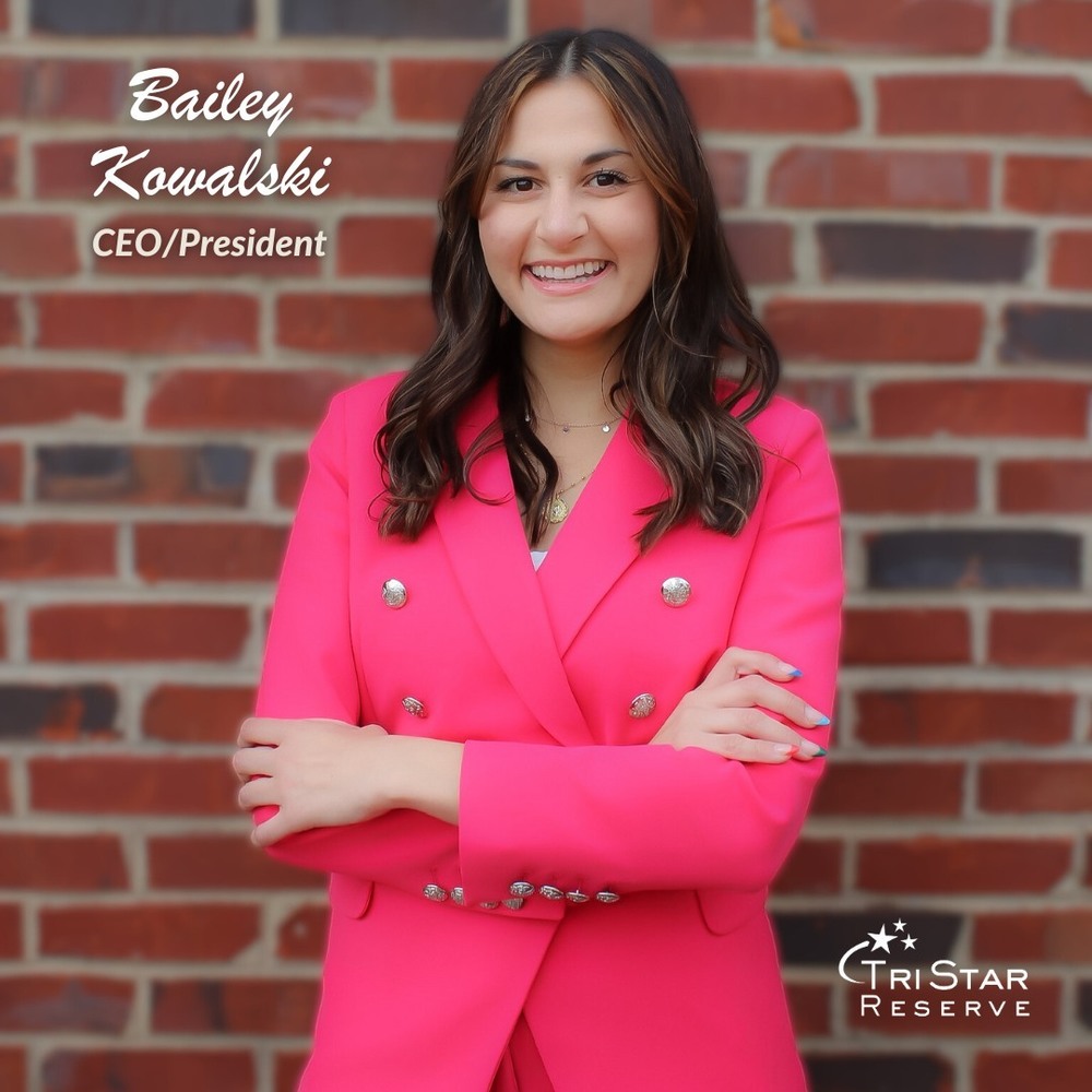 A women standing against a brick wall wearing a bright pink business suit smiling
