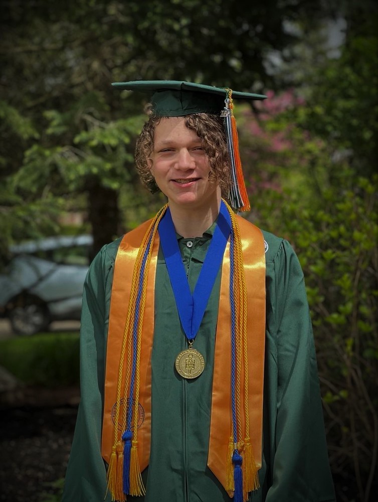 Picture of a man wearing a green graduation gown with a yellow stole and a medal