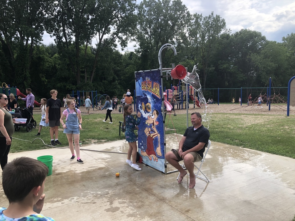 teacher sitting under splash bucket with children standing around