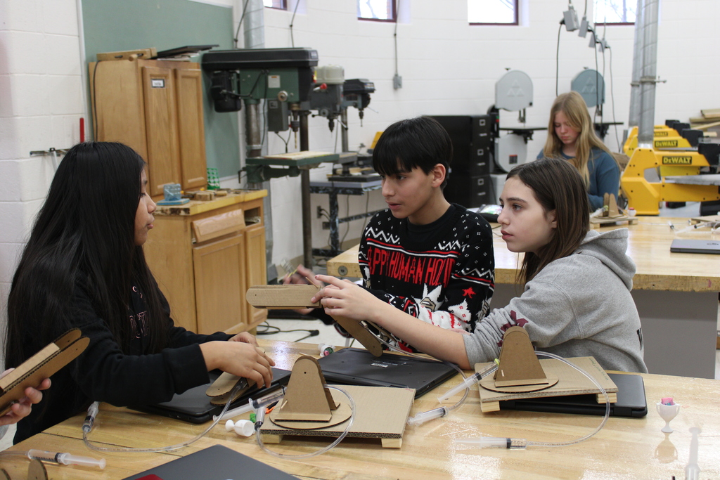 three students discussing a robot arm at a table