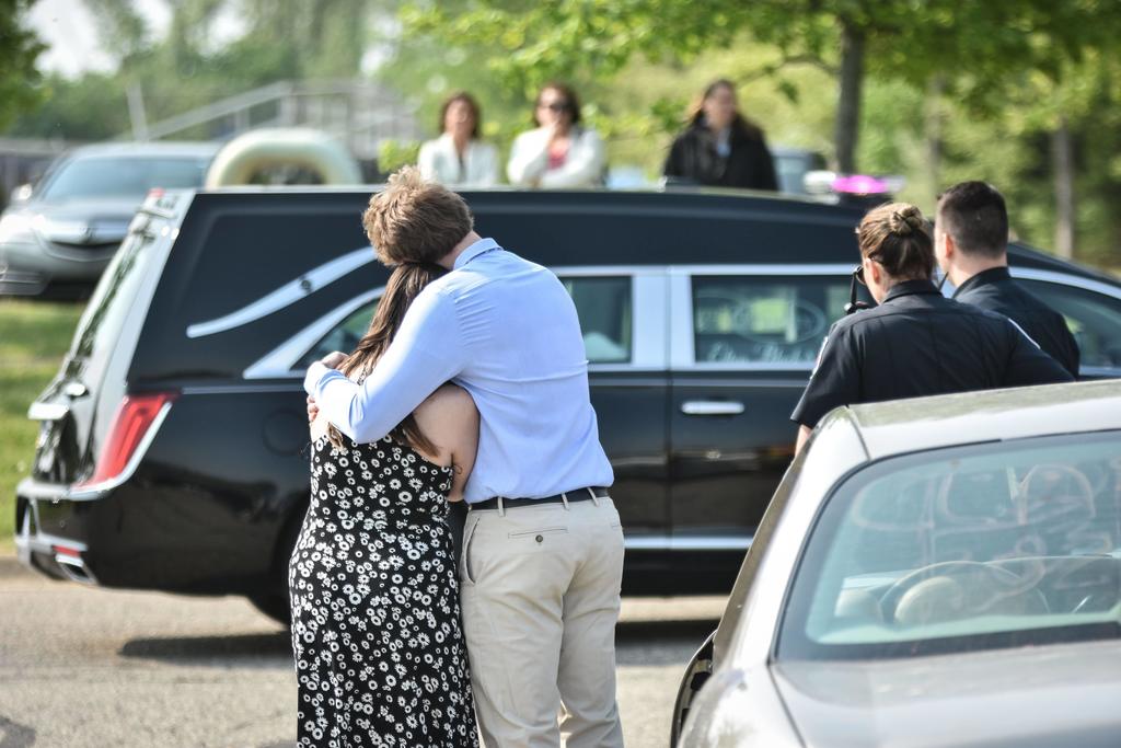 Students hugging in front of a hearse with two police officers standing next to them. 